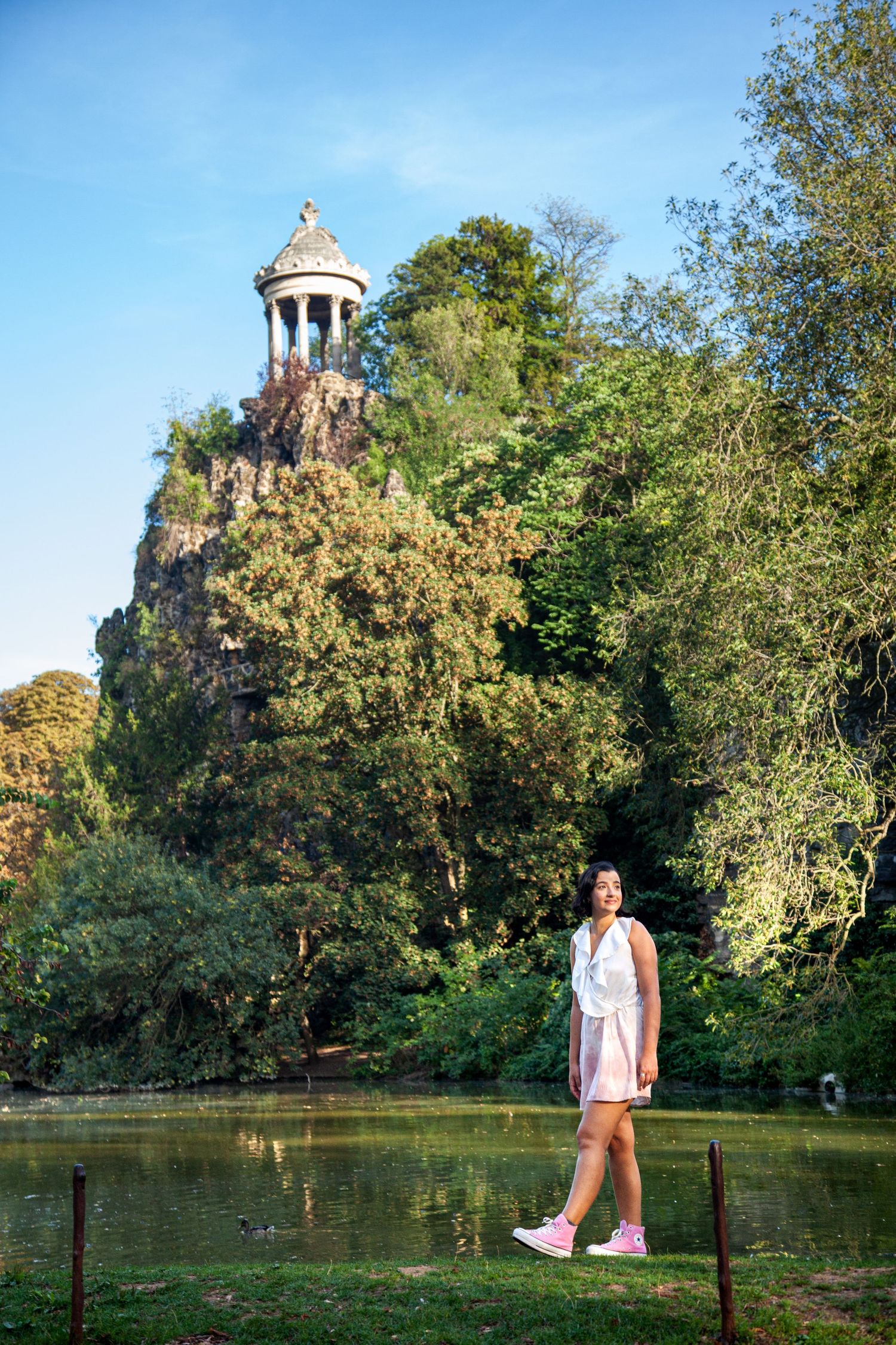 Historic stone temple perched atop a hill overlooking a serene pond in a public park.