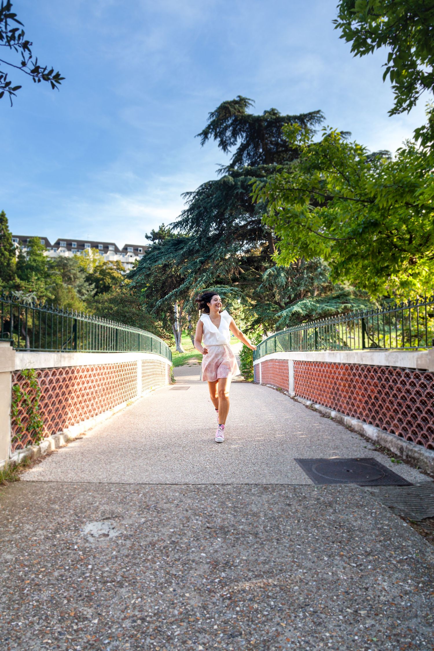 Sun-drenched footbridge path with decorative railings surrounded by lush park scenery.