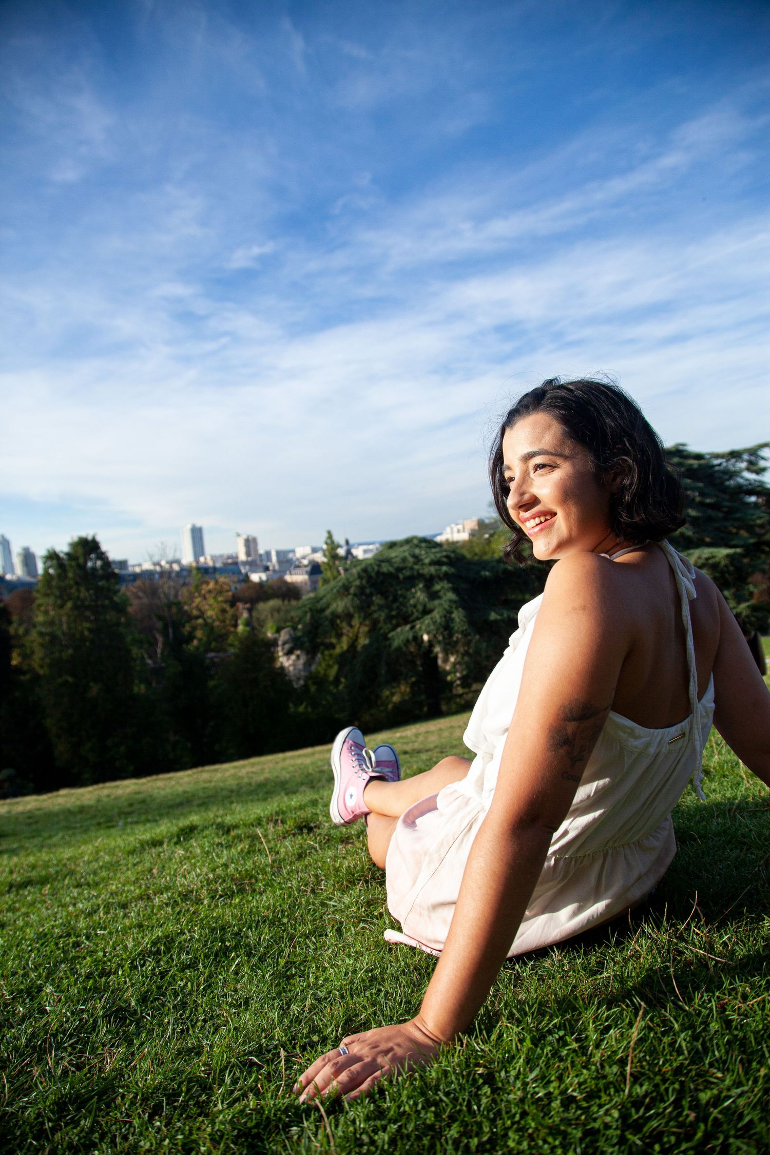 Grassy hillside overlooking city skyline on sunny day with trees in foreground.