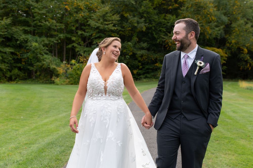 Newlyweds laugh together during outdoor wedding portraits on a lawn with autumn trees in the background.