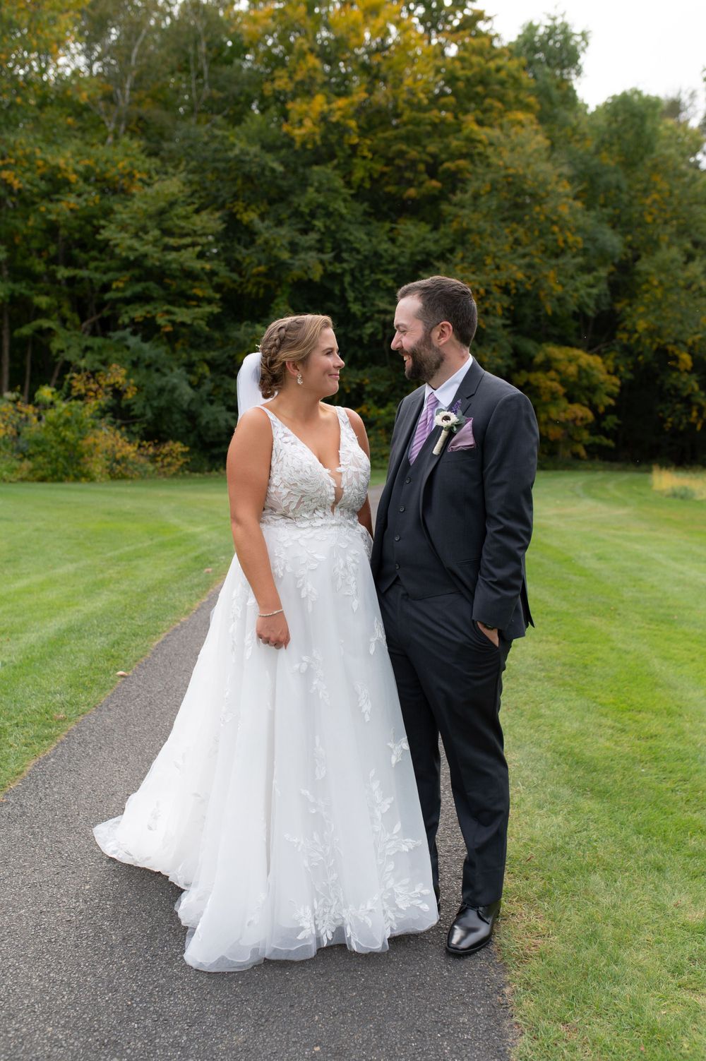 Elegant couple shares a moment on a paved path with autumn trees in background.