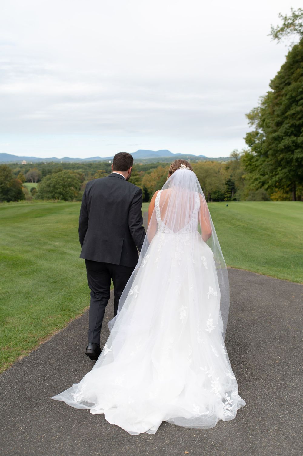 Couple walks down path with flowing white wedding dress trailing behind.
