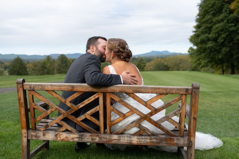 Couple shares intimate moment on wooden bench overlooking scenic landscape.