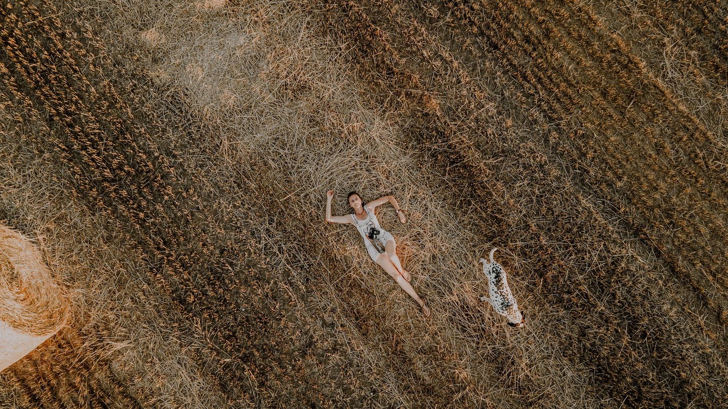 Aerial view of two people lying in geometric patterns on plowed agricultural field.