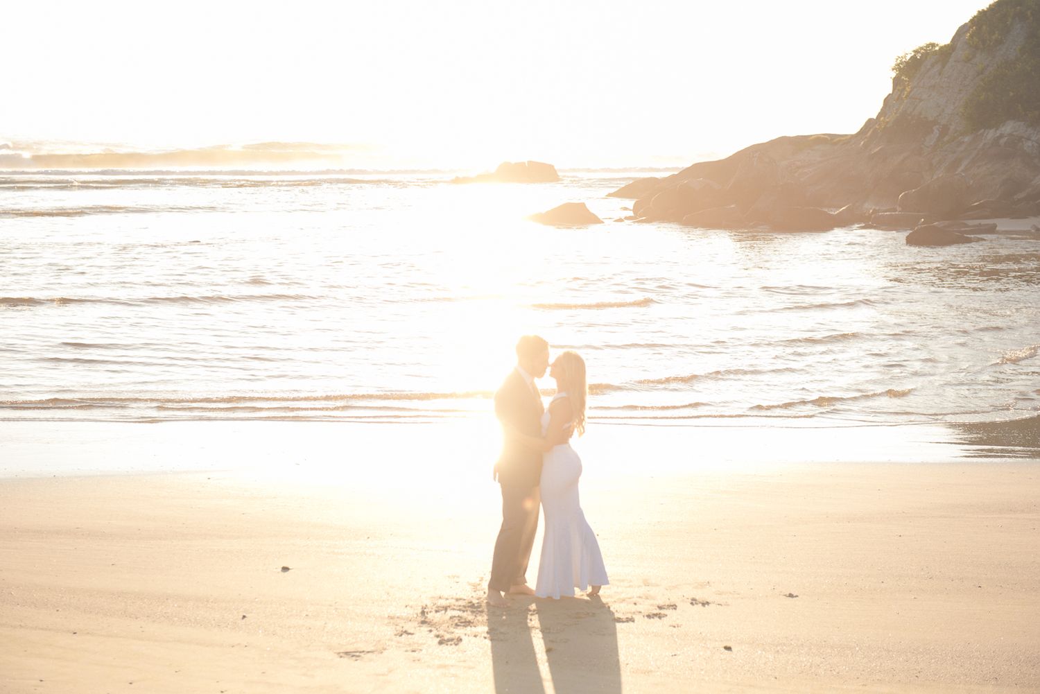 A romantic silhouette of a couple embracing on a sunset beach with golden light streaming through the scene.