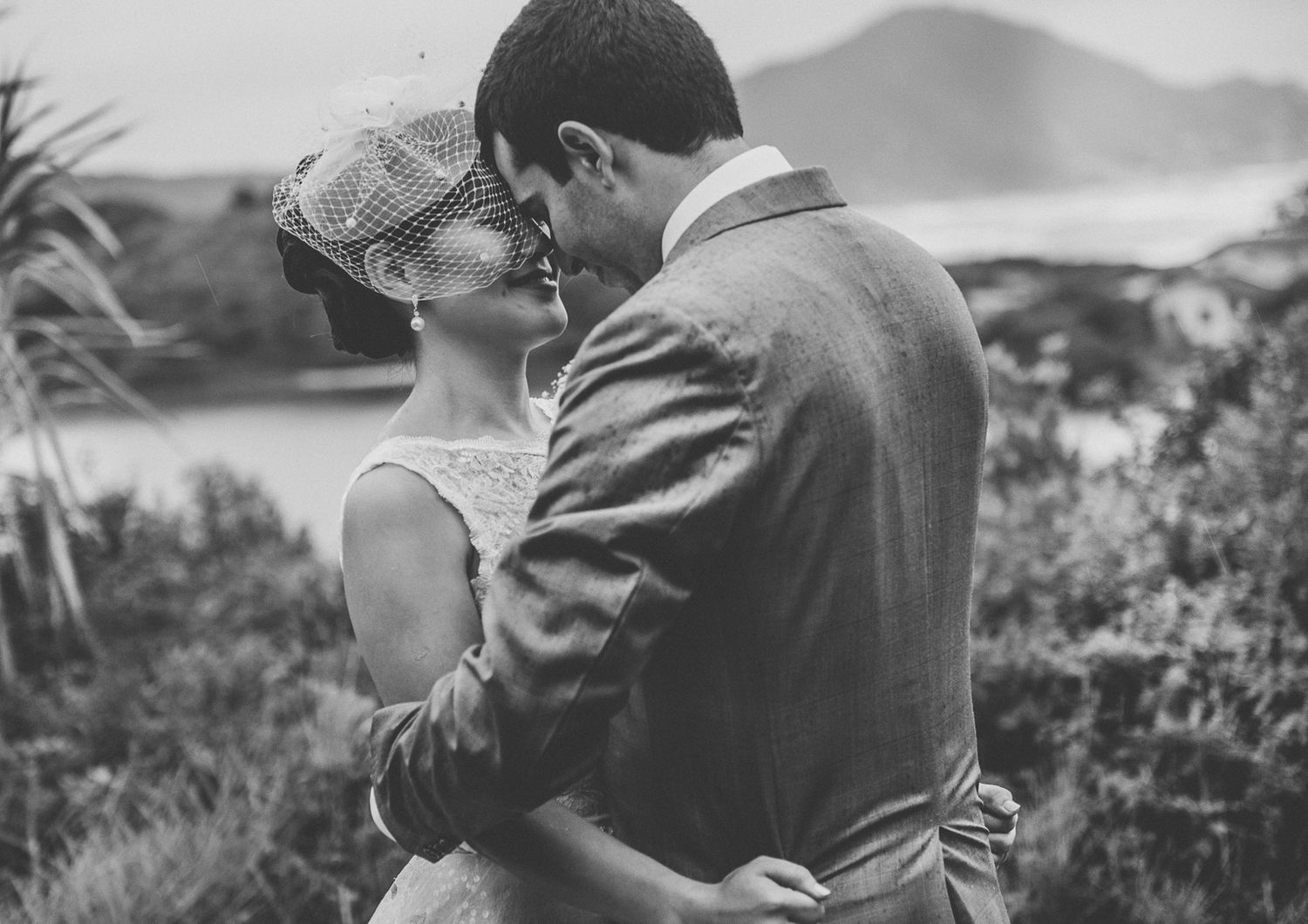 A black and white portrait capturing a tender moment between newlyweds against a mountain backdrop.