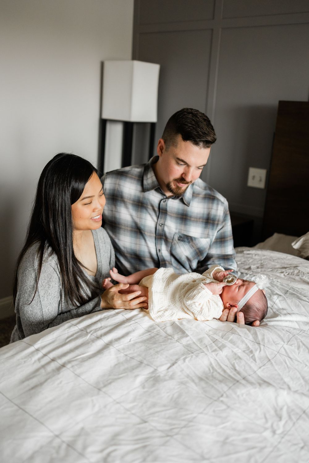 A couple tends to their newborn baby while sitting on a bed with white linens.