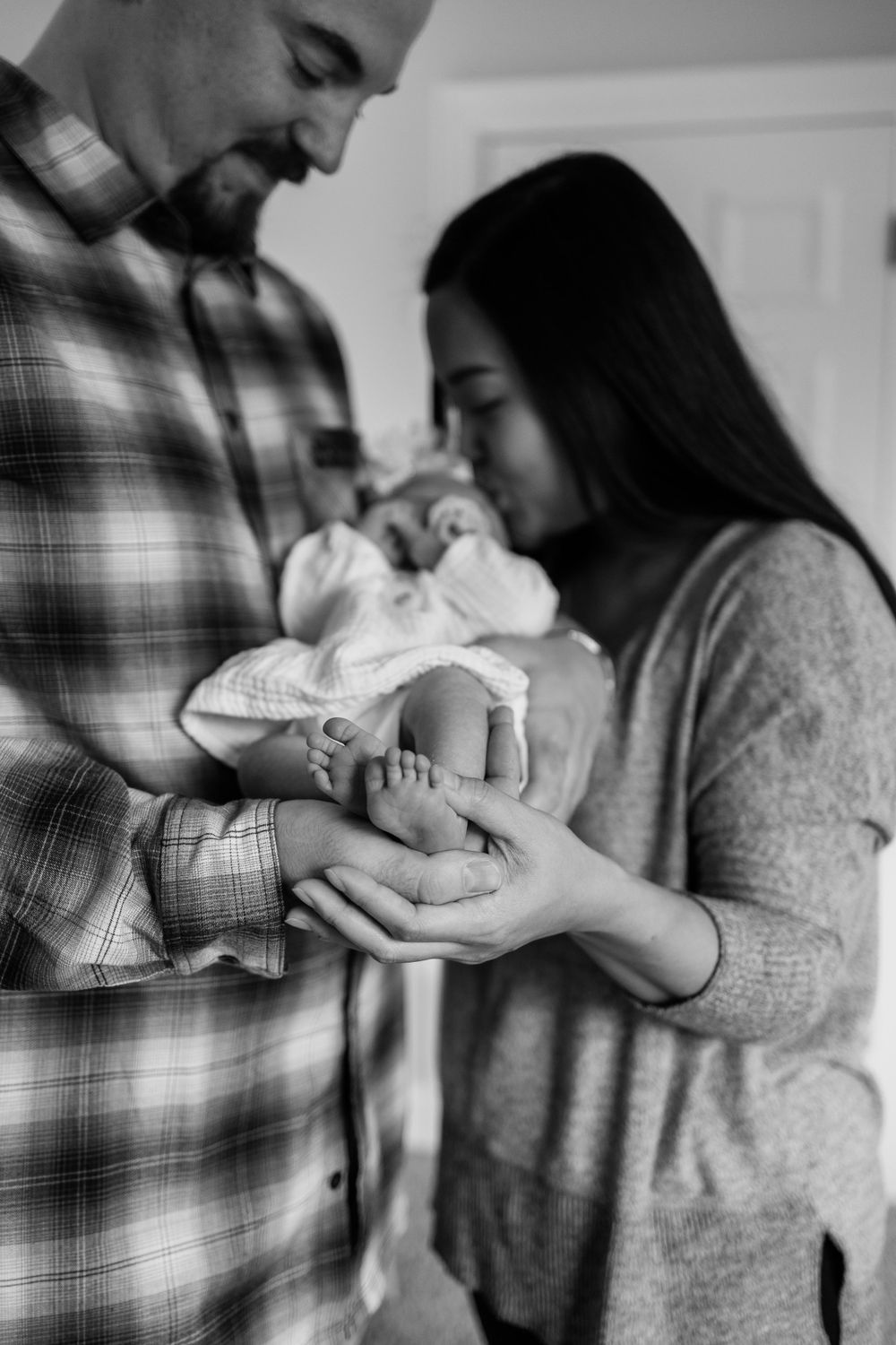 An intimate black and white portrait of new parents gazing at their newborn.