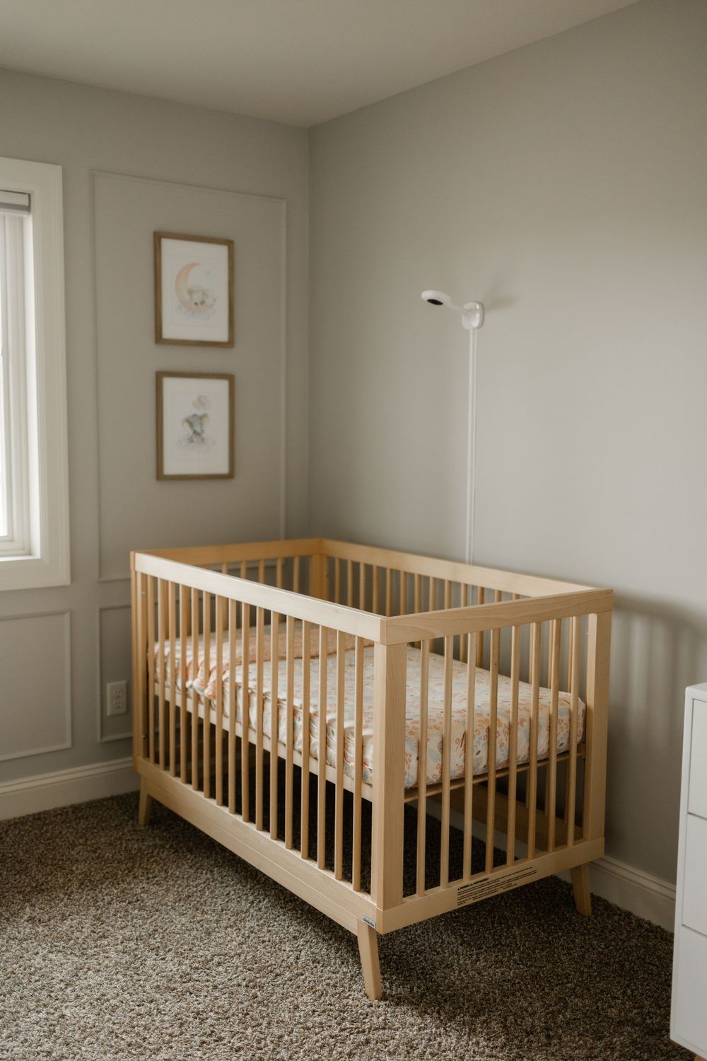 A minimalist nursery with wooden crib, gray walls, and framed artwork.