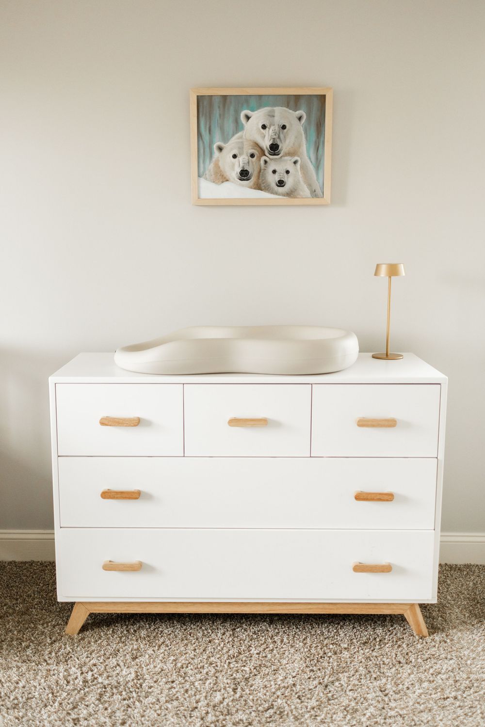 White modern dresser with changing pad and polar bear artwork in minimalist nursery.