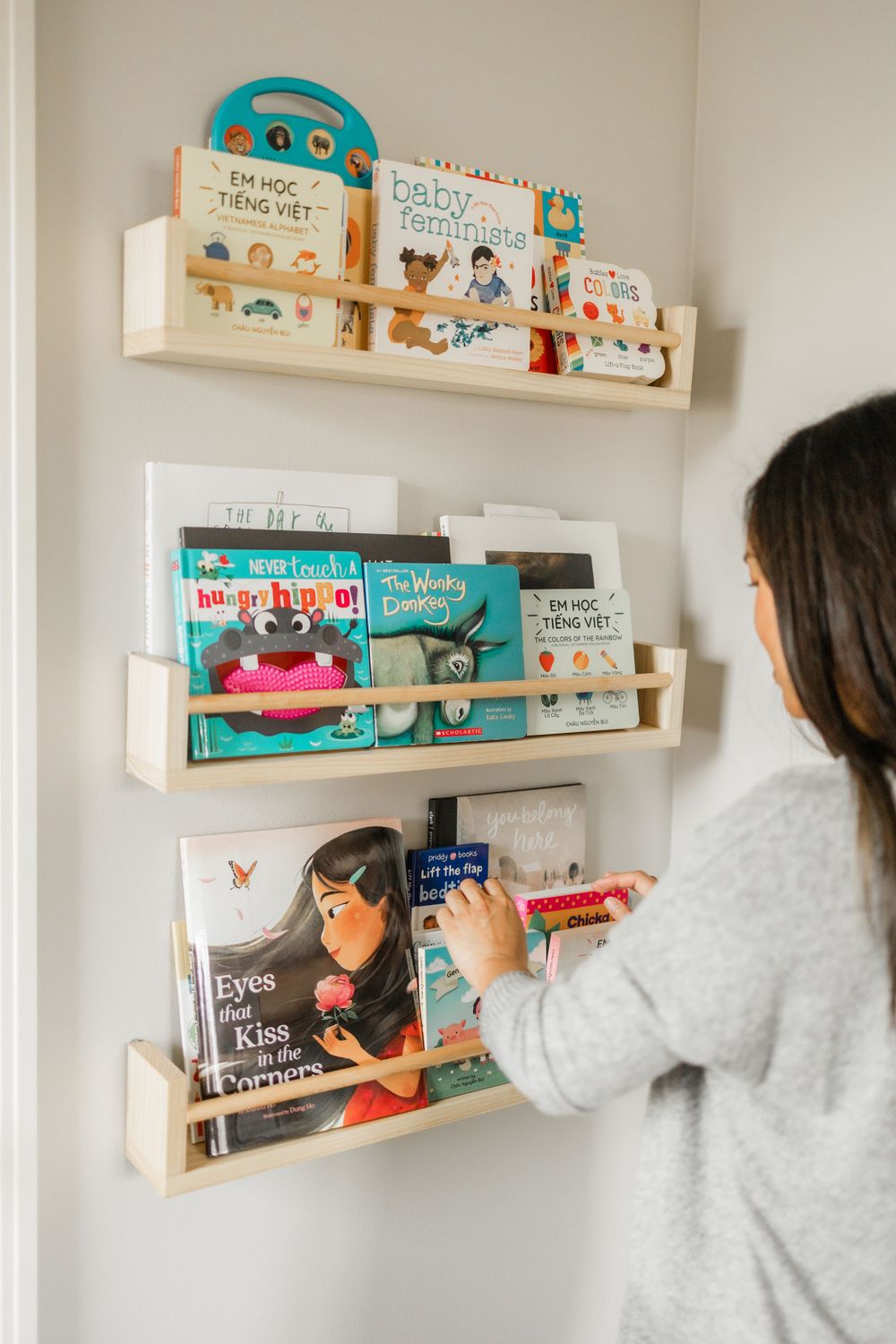 Wall-mounted wooden book shelves displaying colorful children's books in nursery.