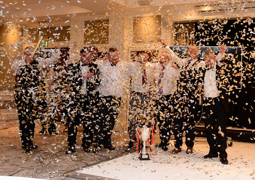 Celebration scene with confetti raining down on formally dressed group in elegant ballroom.