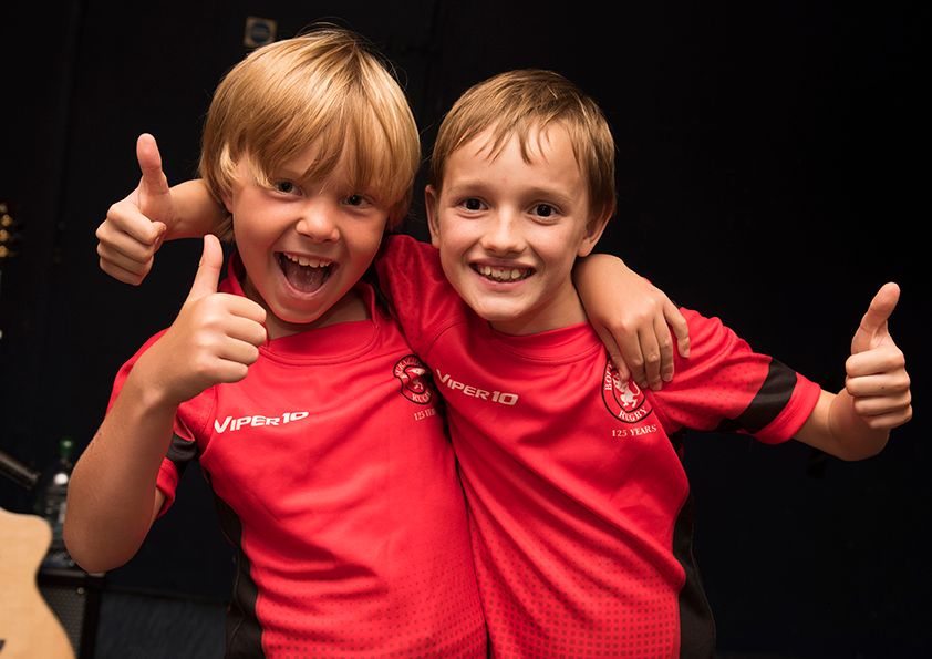 Two young boys in matching red shirts giving enthusiastic thumbs up.