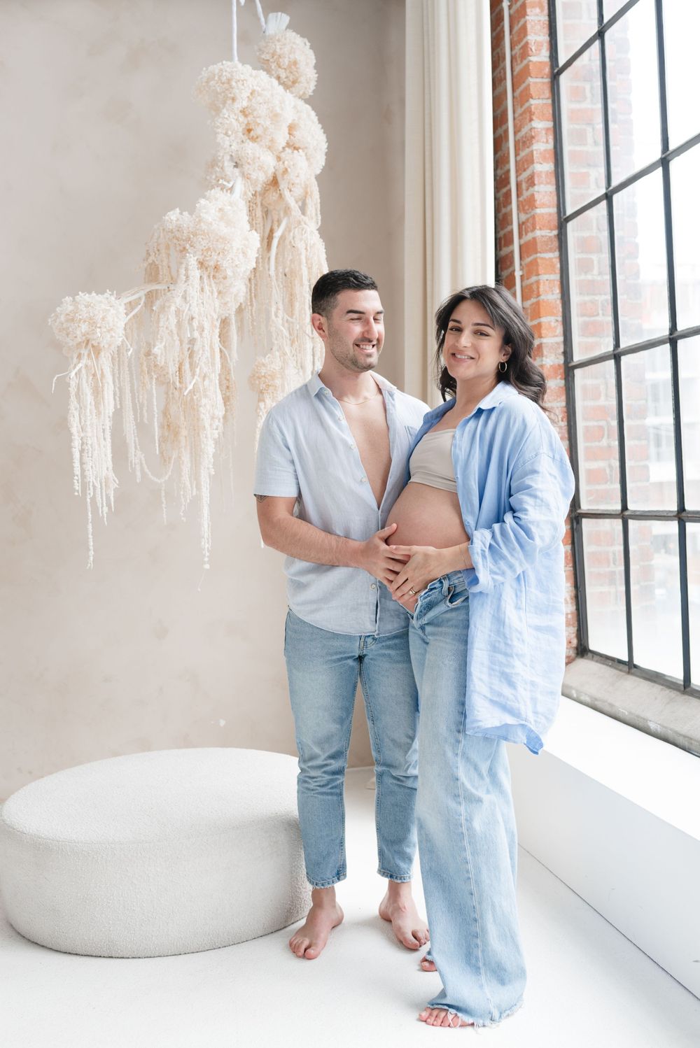 Couple smiling and holding baby bump for maternity photoshoot in light and airy background at toronto mint room studios