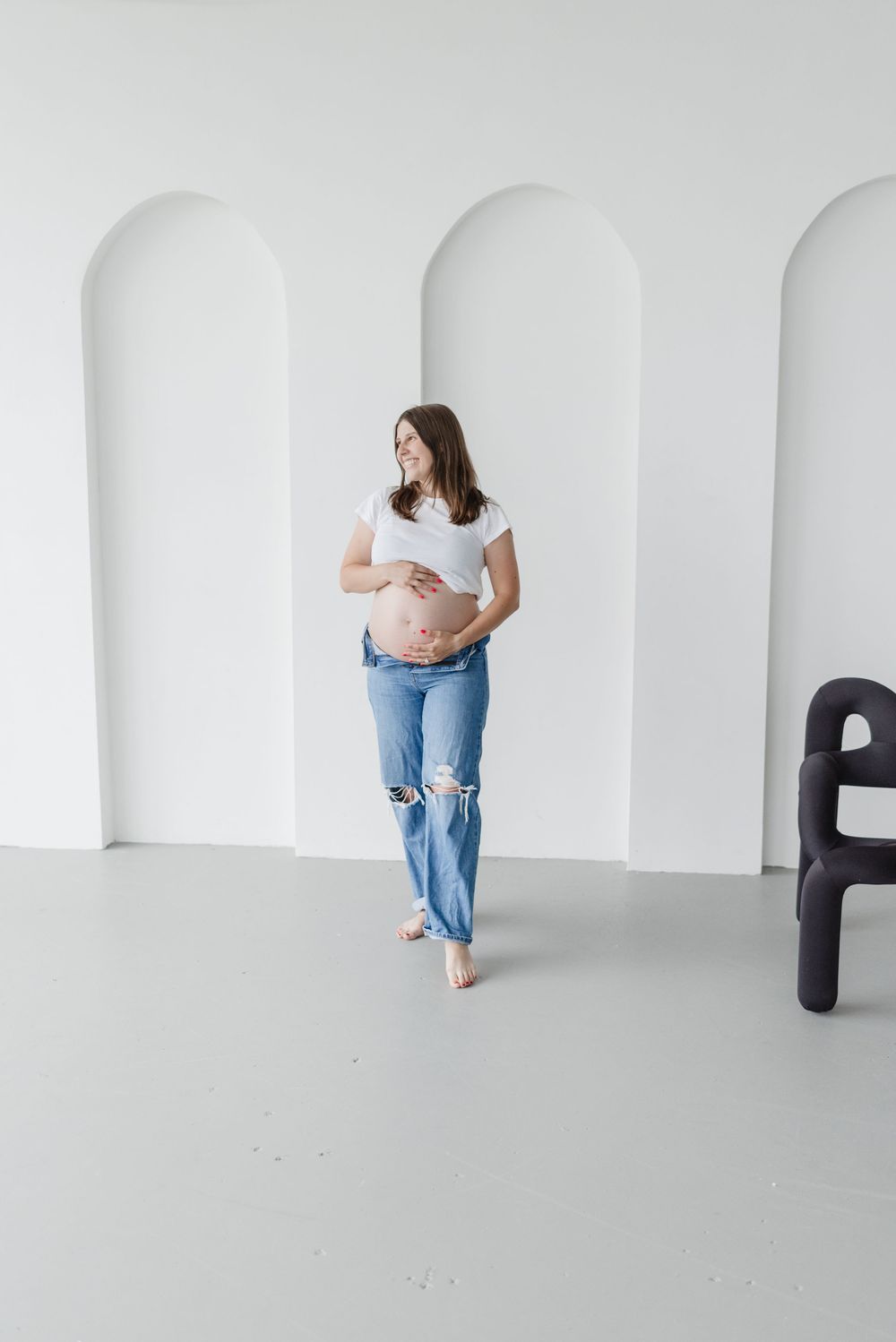 Pregnant woman holding her baby bump wearing casual jeans and white shirt for a toronto maternity photoshoot at Icon Studio Space
