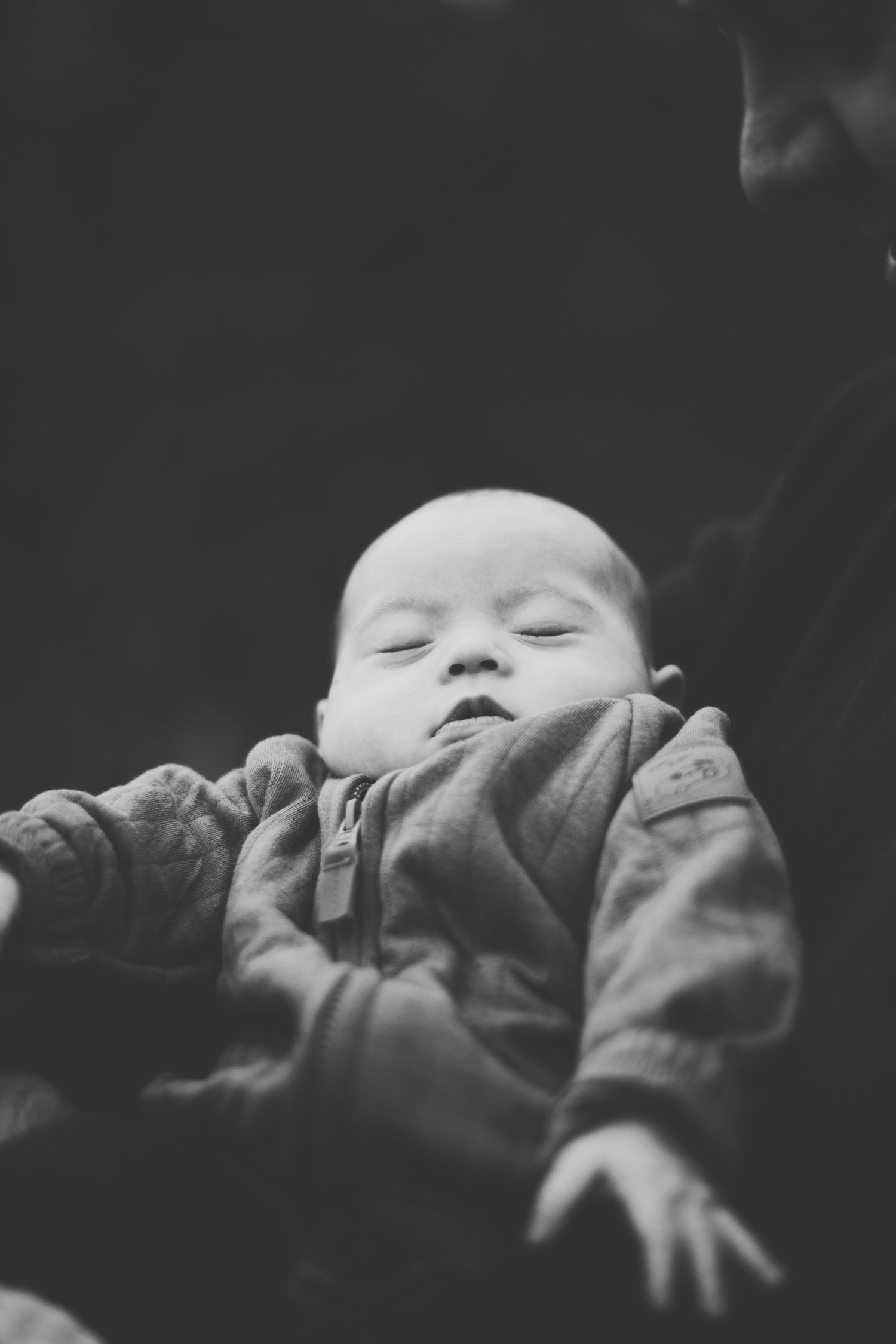 A sleeping baby in a winter jacket captured in black and white photography.