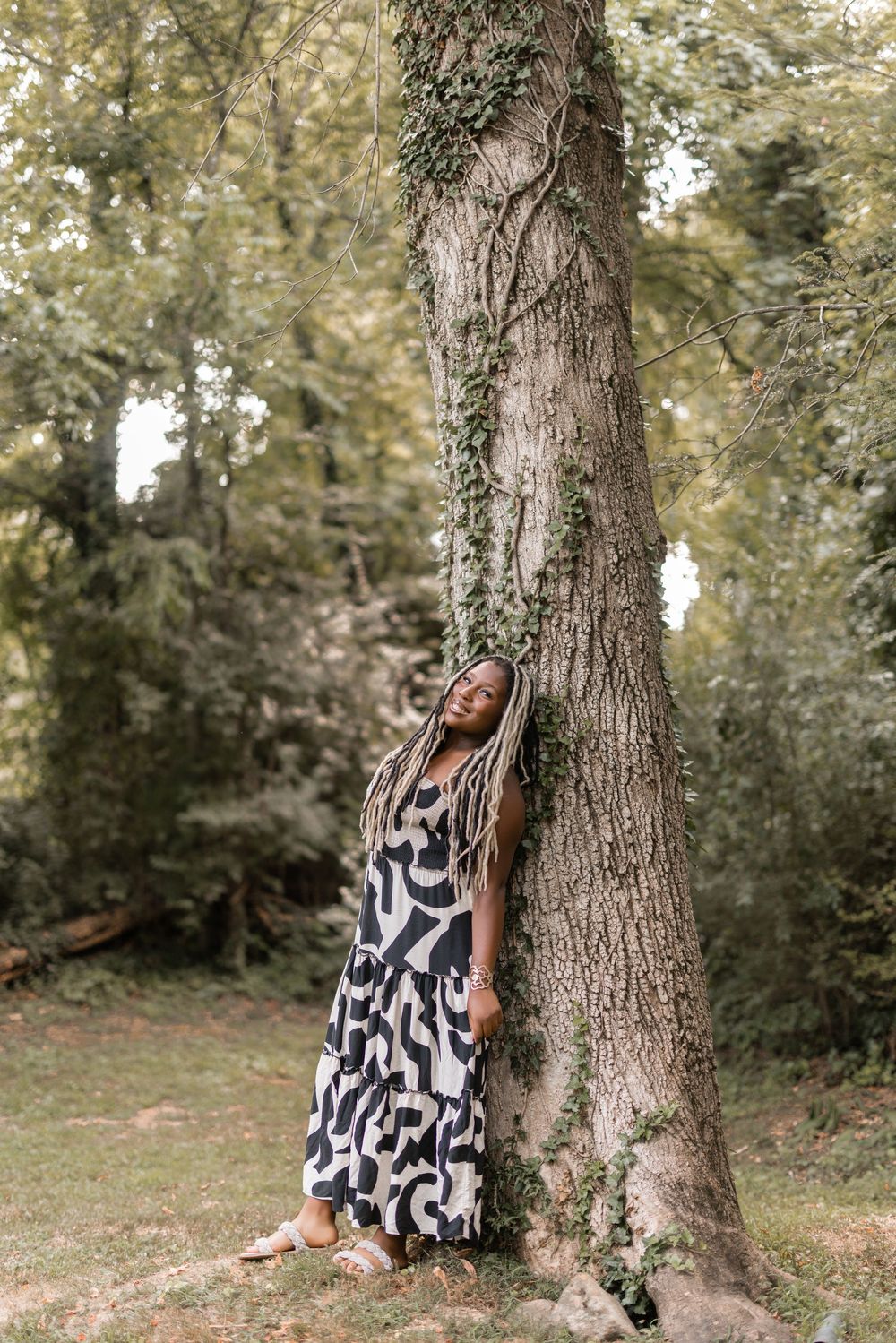 A dreamy outdoor photo series of a woman in a black and white patterned dress posing against a large tree trunk.