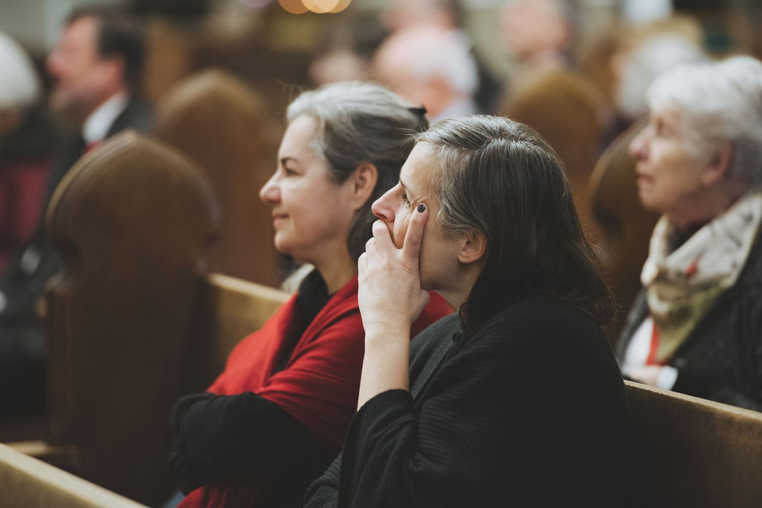 People sitting in church pews during a service with thoughtful expressions and contemplative poses.