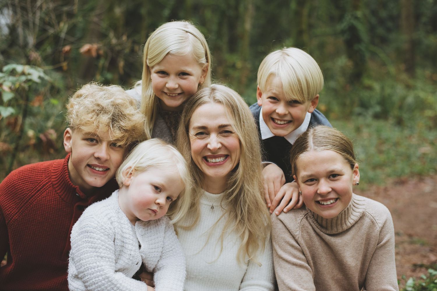 Mother poses with her five children in goldstream provincial park while wearing festive cosy sweaters.