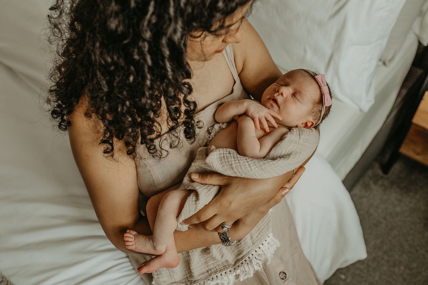 A tender moment captured between parent and newborn baby on white bedding in soft natural lighting.