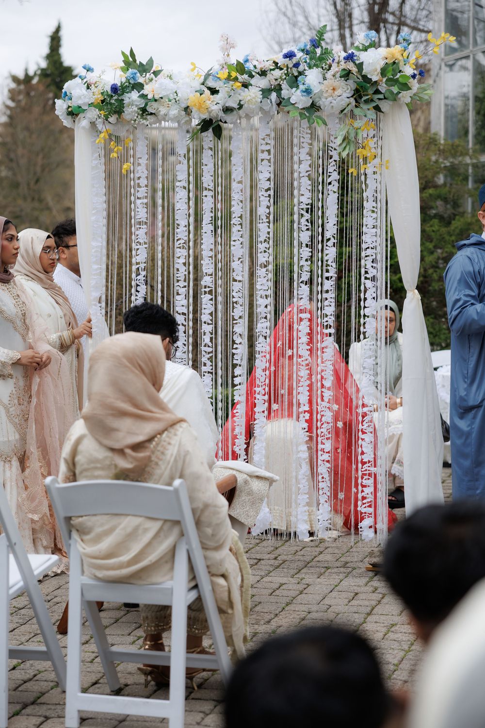 Wedding arch decorated with white flowers and hanging crystals at an outdoor ceremony.