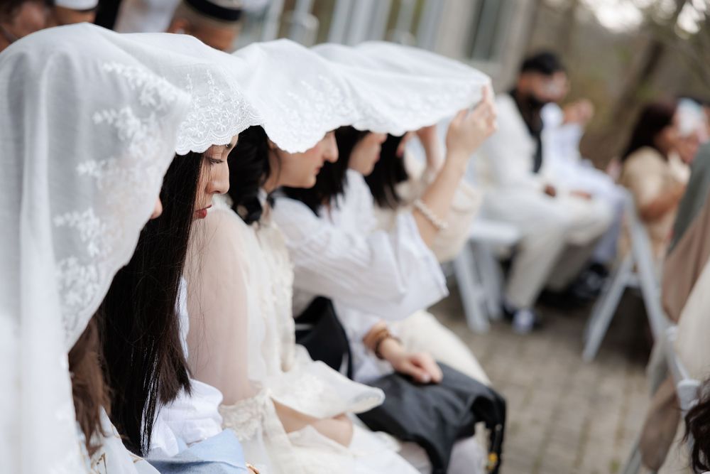 Wedding guests seated in white chairs during an outdoor ceremony.