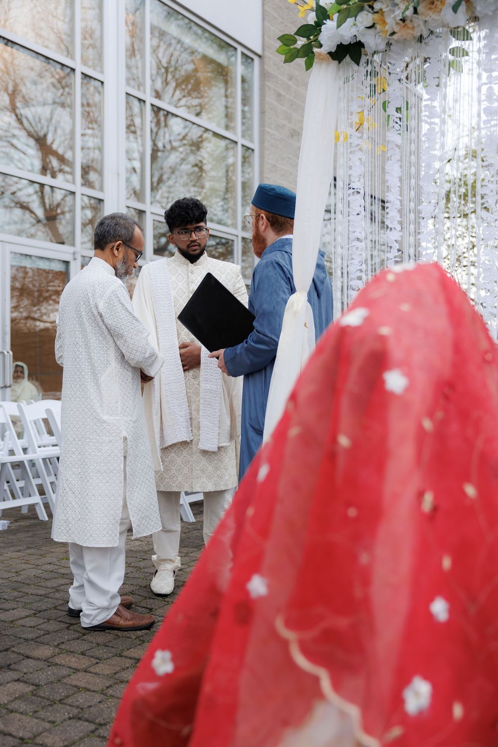 Wedding ceremony in progress with guests and officiants gathered under decorative arch.
