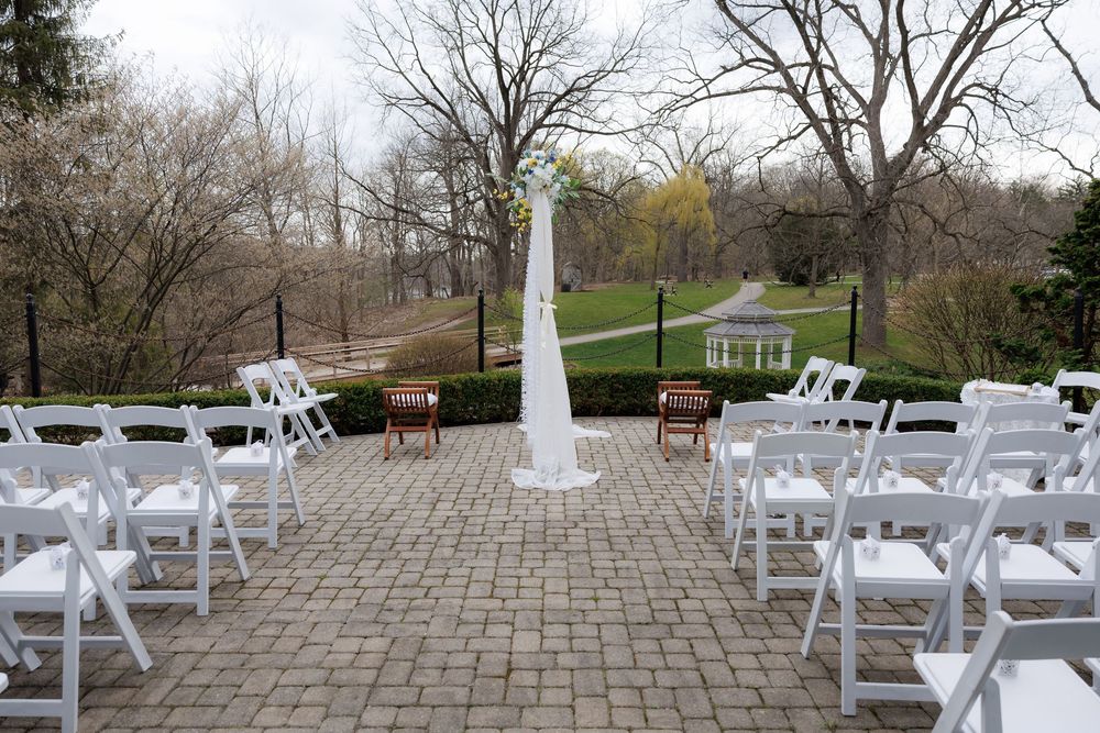 Outdoor wedding ceremony setup with white chairs and arch on a stone patio.