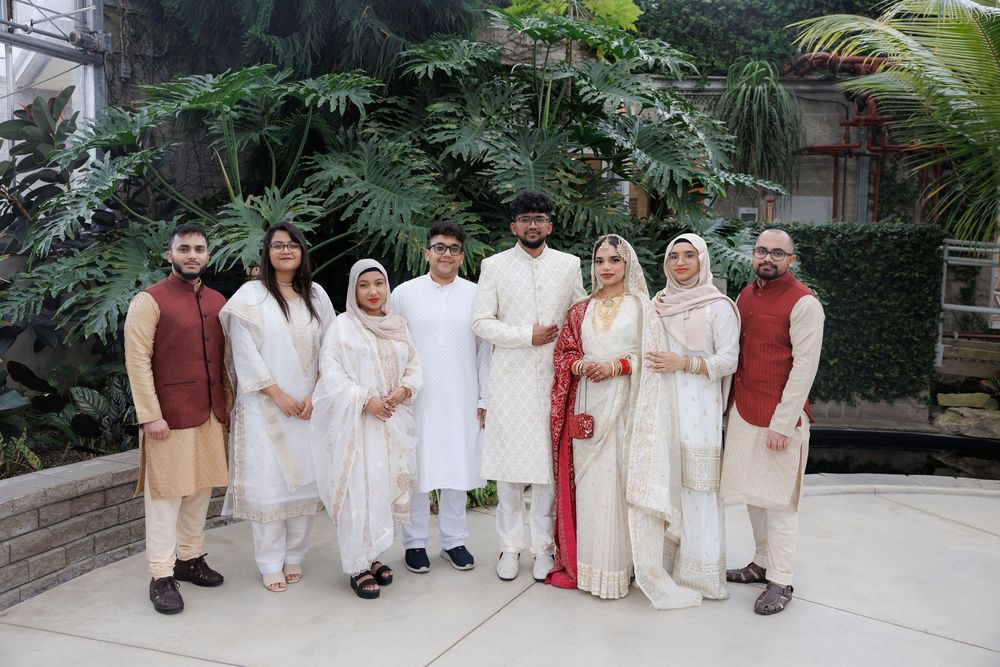 Family group wearing traditional South Asian wedding attire in white and red poses together in a garden setting.