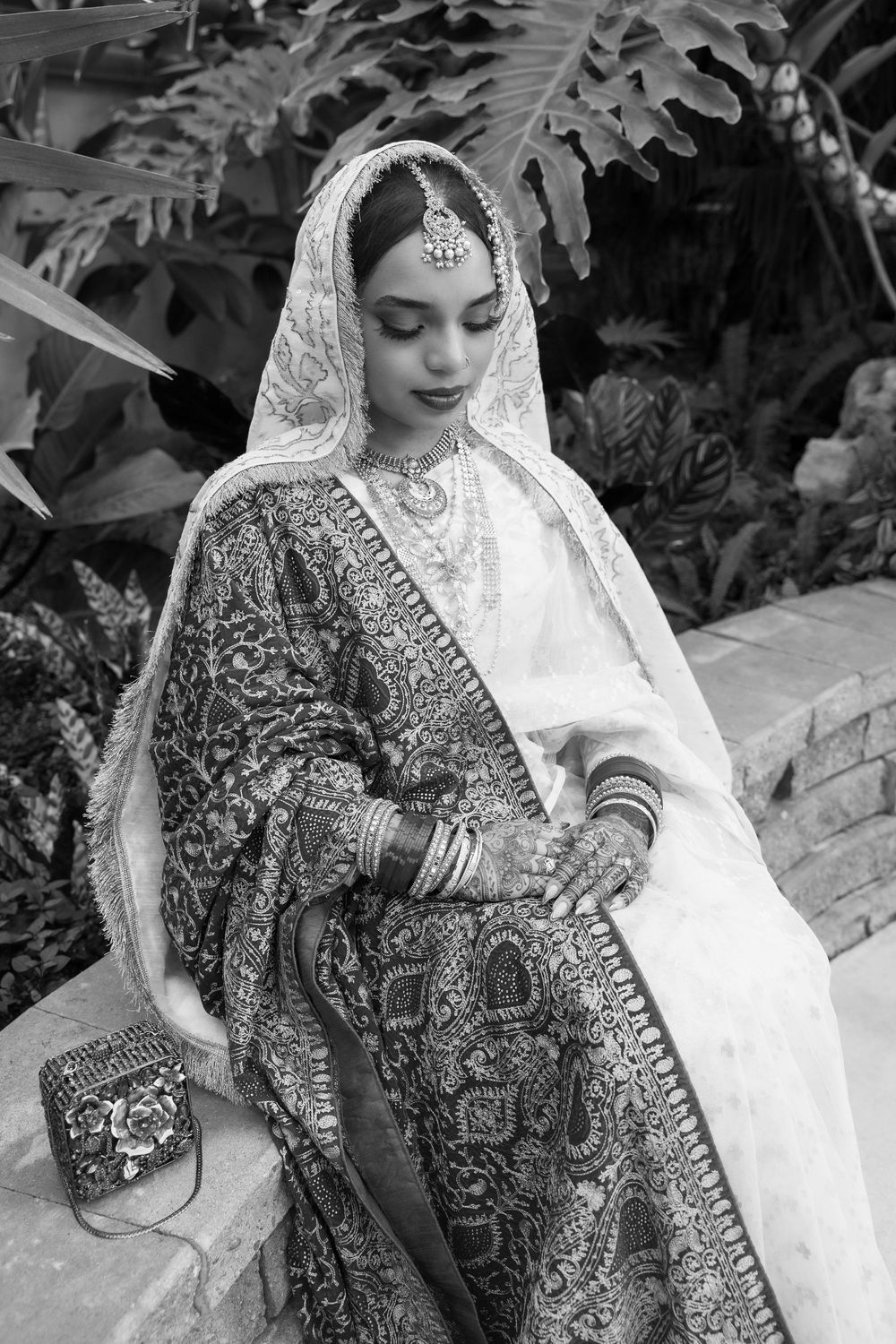 Black and white portrait of bride in ornate South Asian wedding attire with detailed embroidery and jewelry.
