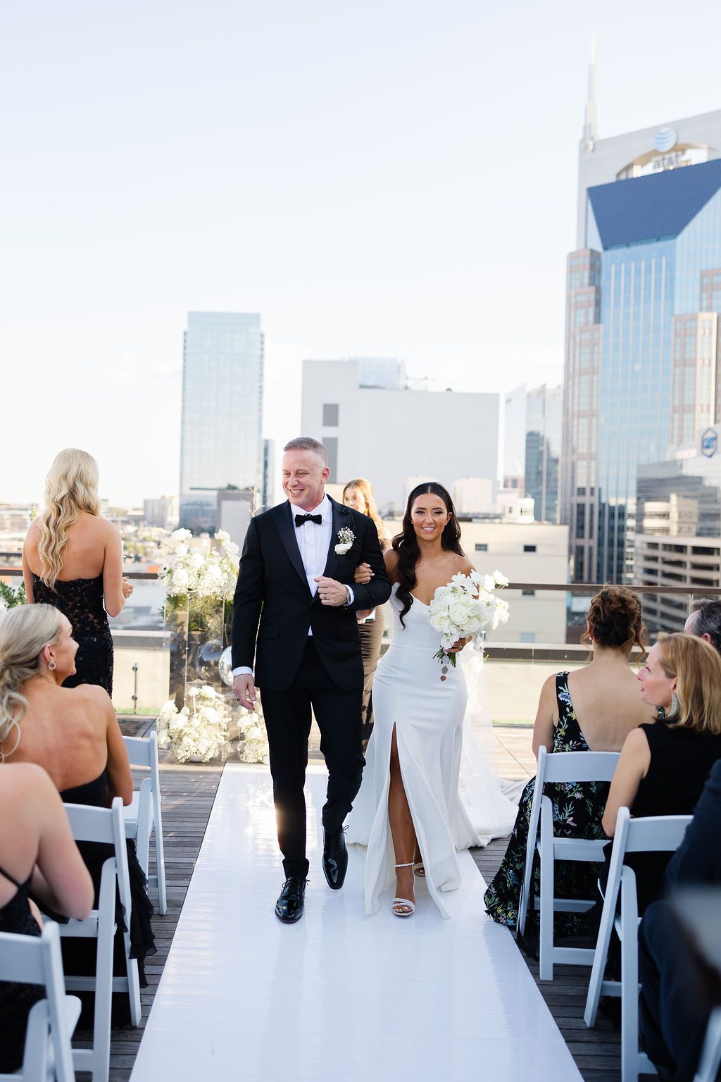 A couple walks down a white aisle during a rooftop wedding ceremony with Nashville city skyline in the background. Top 10 Nashville Wedding