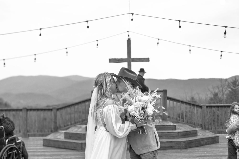 Black and white photo of wedding ceremony on rustic deck with mountain landscape.