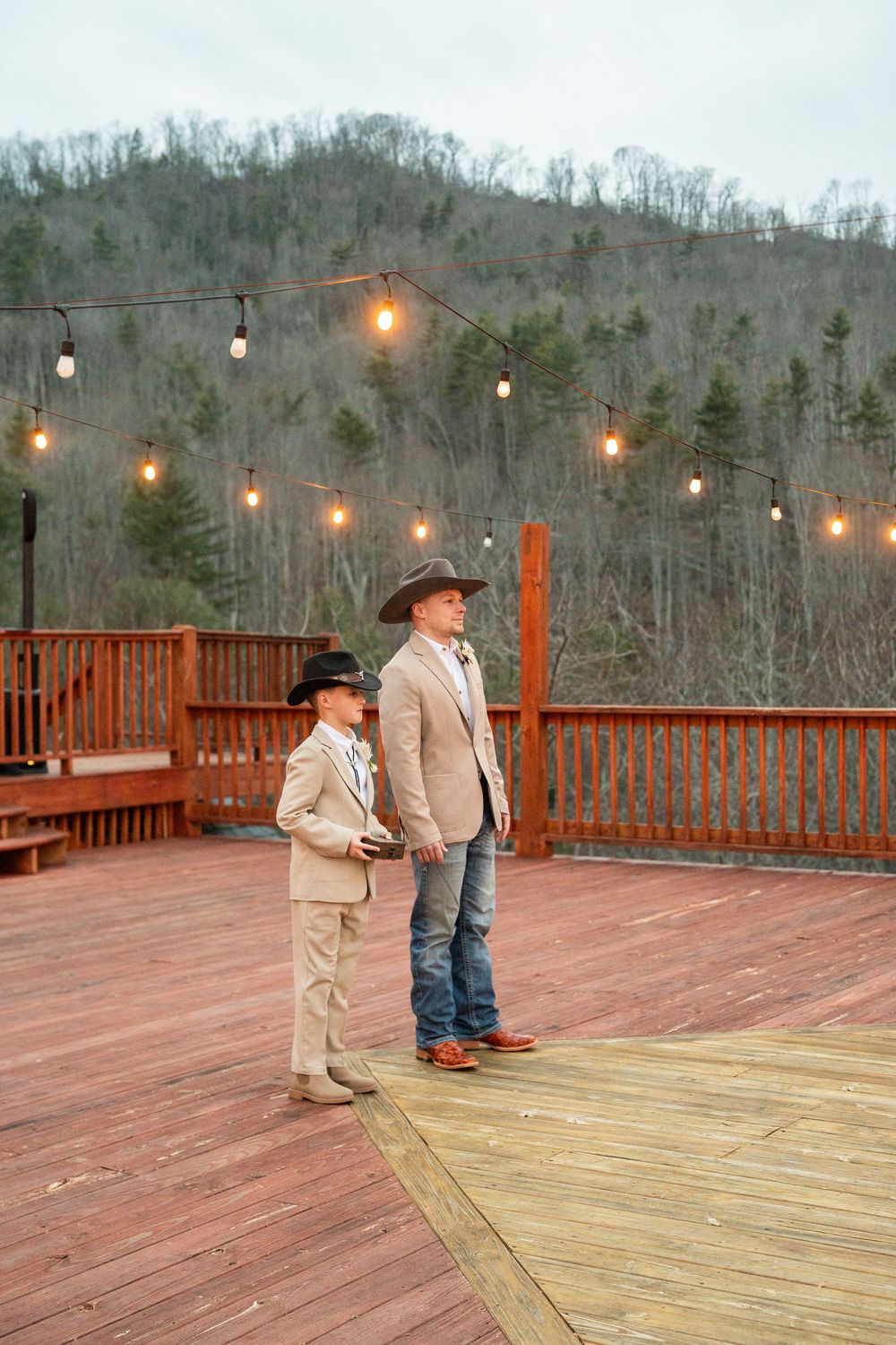 Log cabin wedding venue deck decorated with string lights overlooking mountain views at dusk.