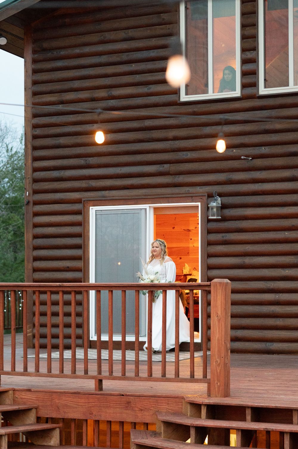 Wooden log cabin exterior with wrap-around deck and string lights during an evening event.