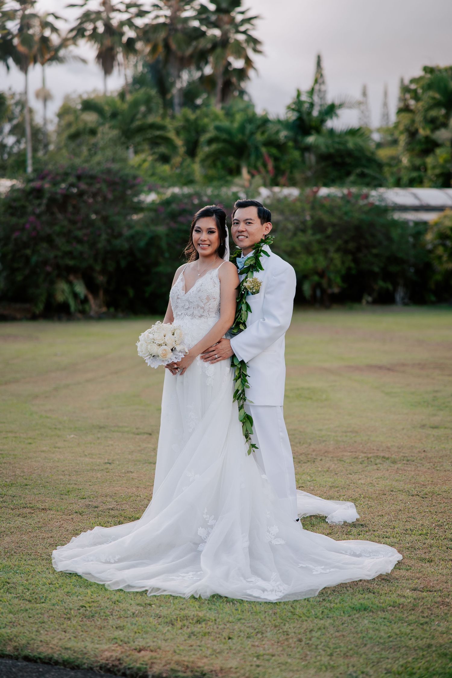 Bride and groom smiling at the camera after their ceremony, with the bride holding her bouquet and the groom holding her waist in Hilo, HI.