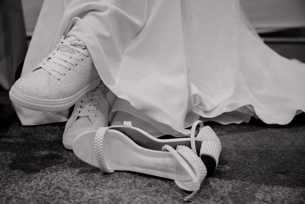Black and white shot of white sneakers and dress fabric on the floor with one shoe laid sideways.
