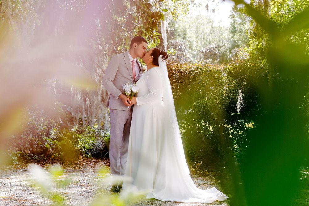 A romantic couple embraces in a sunlit garden setting with green foliage and dreamy lighting effects.