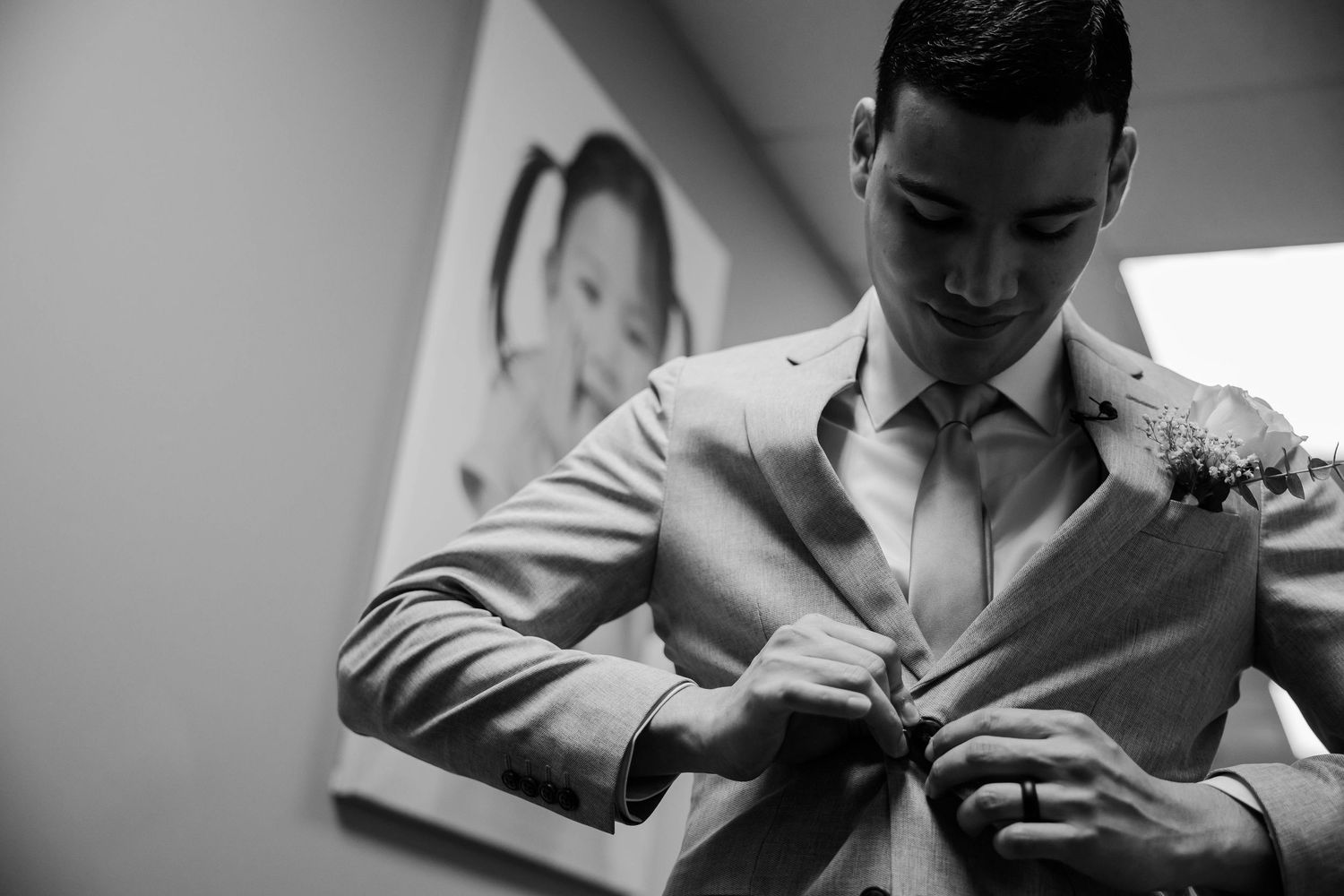 A person in formal attire buttoning up a light-colored suit jacket in a black and white photograph.