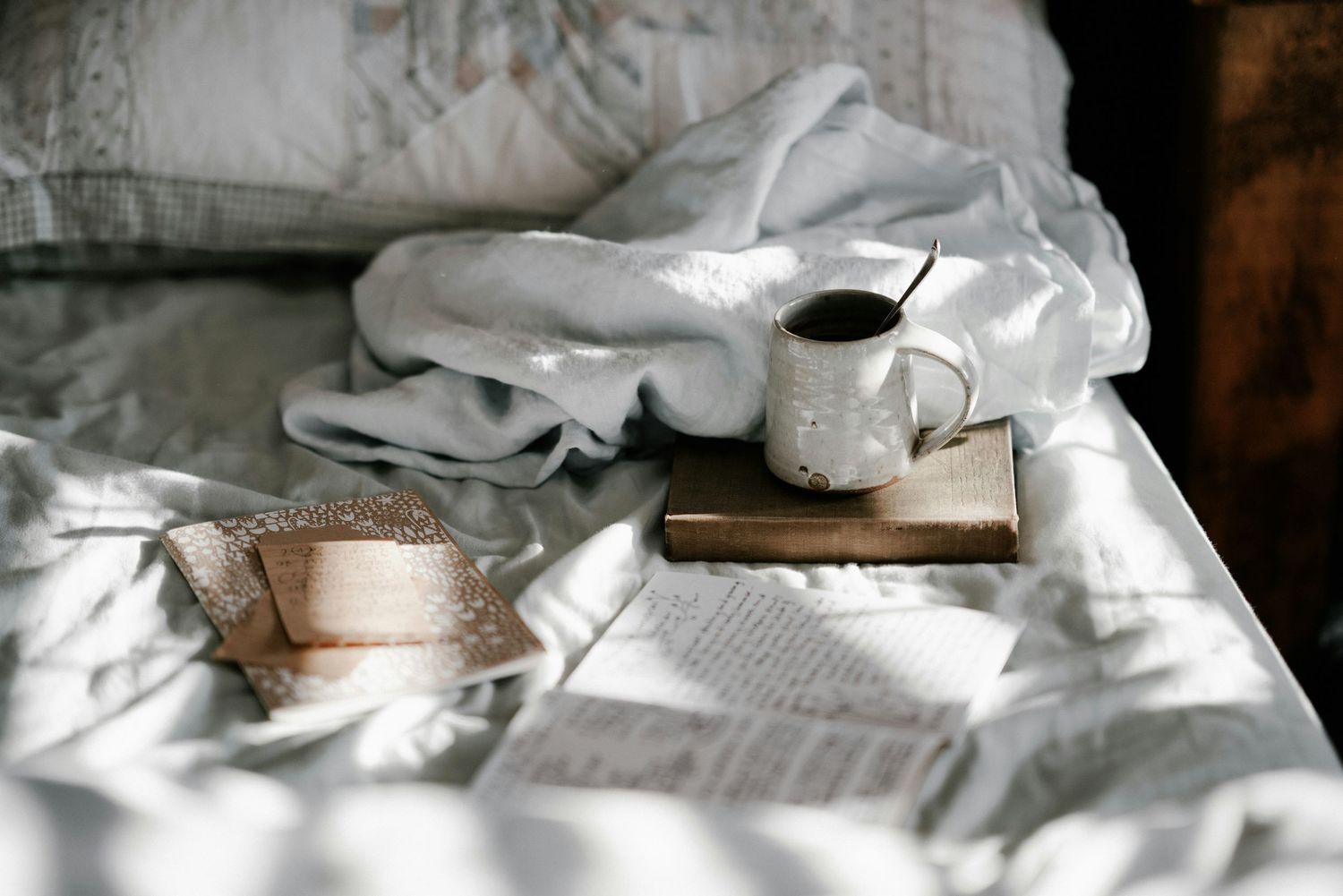 Cozy bed scene with white linens, open book, and morning coffee.