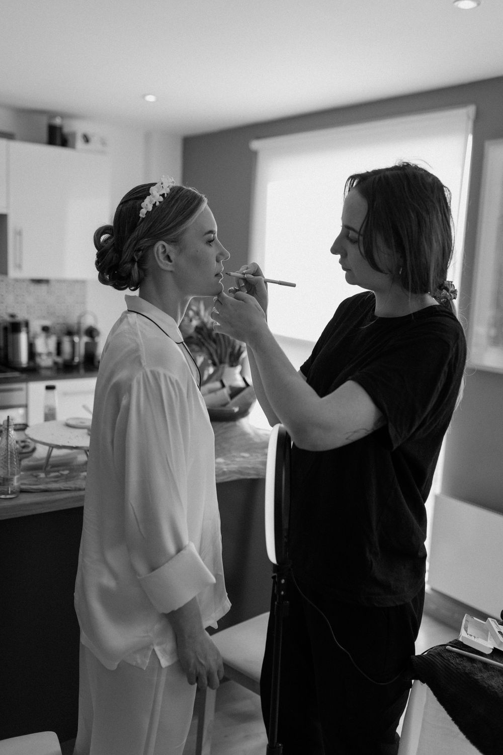 Makeup artist applies cosmetics in black and white photo taken in modern kitchen setting.