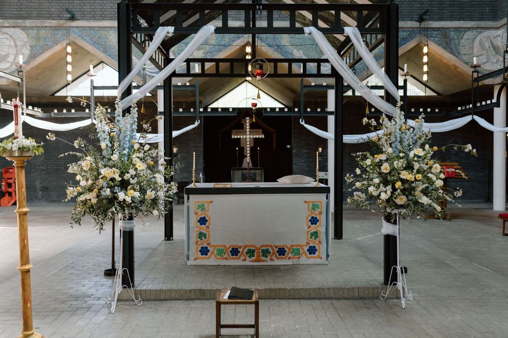 St Paul's Bow Common altar decorated with white floral arrangements and string lights in an industrial venue setting.