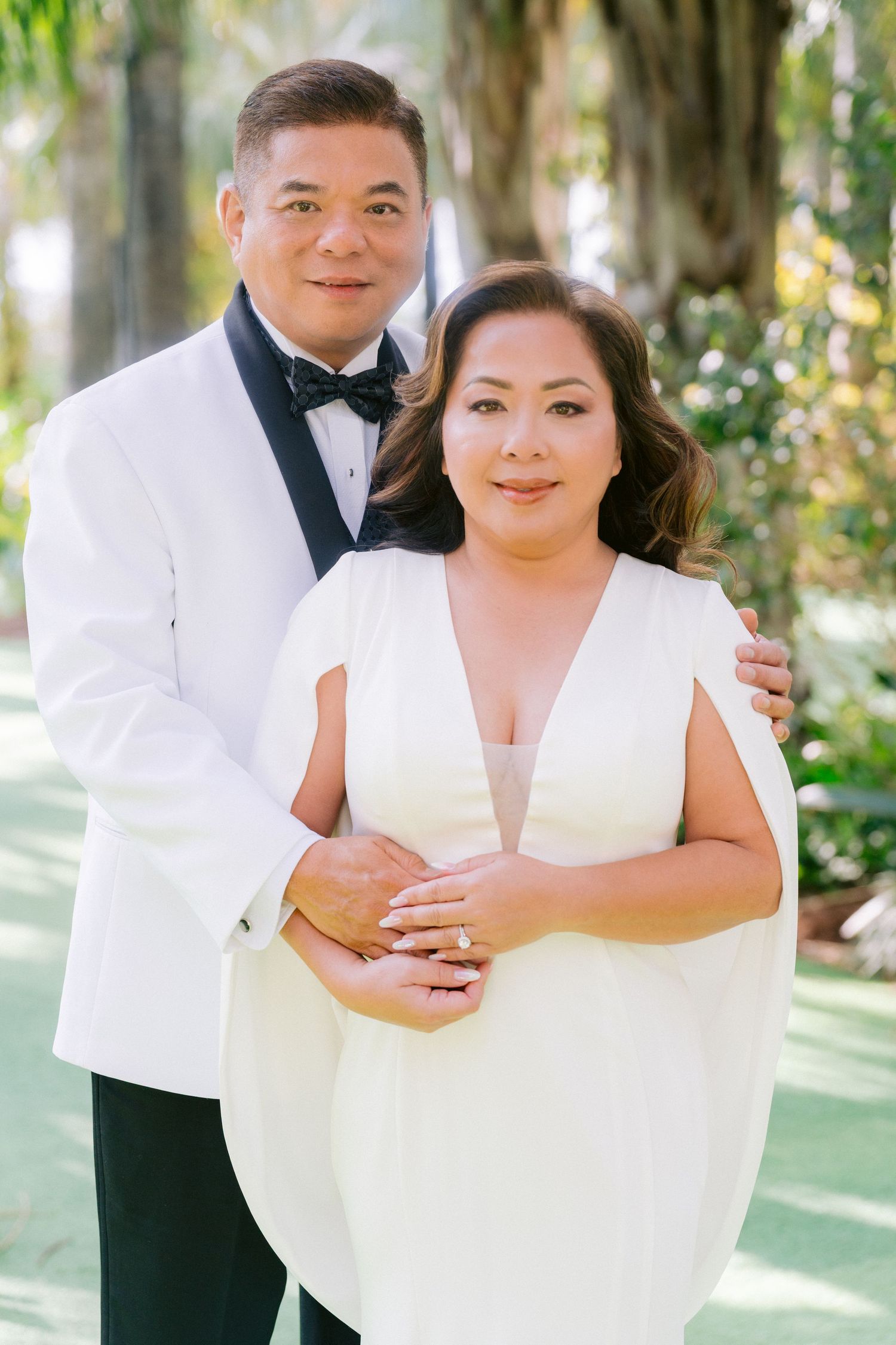 An elegant couple dressed in white formal attire pose together in a romantic garden setting with soft natural lighting. Orlando Florida