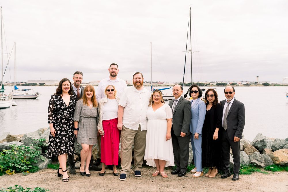 A group stands together by a marina with boats and water in the background on an overcast day.
