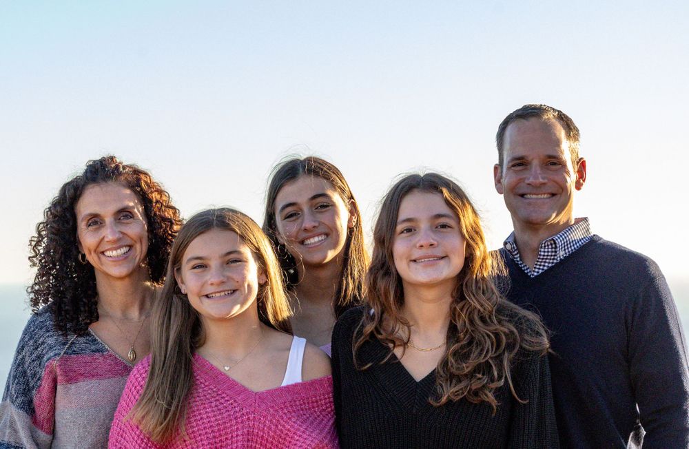 Group of smiling people standing together outdoors against a bright sky background.
