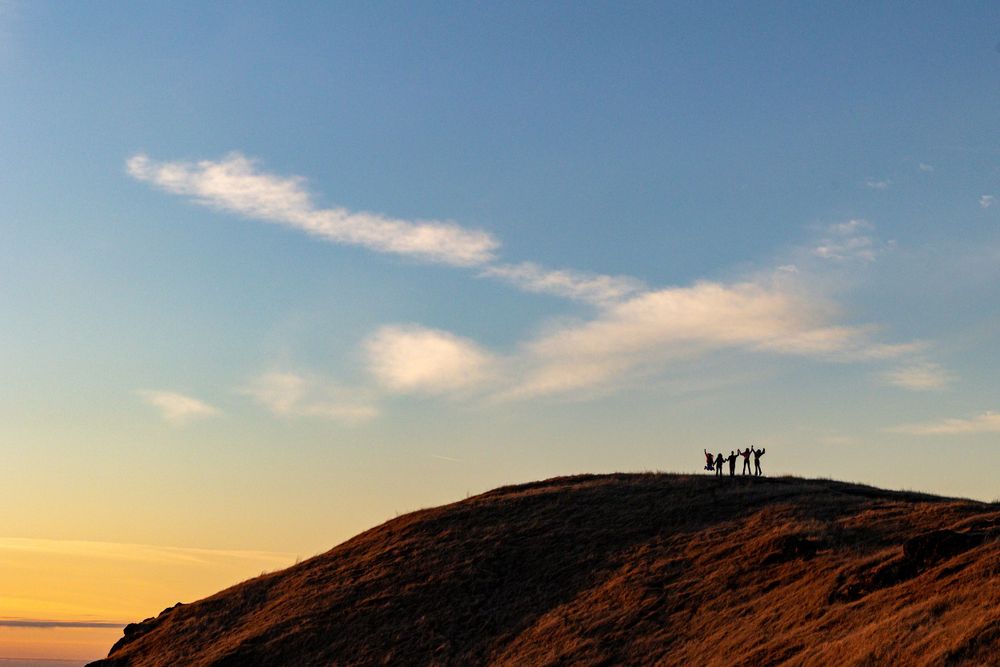 Silhouetted figures stand on hilltop against golden sunset sky with wispy clouds.
