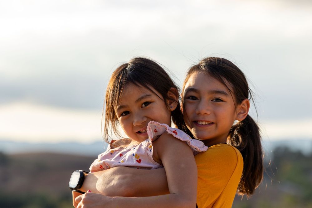 Two young friends smile and hug while enjoying the outdoors at sunset.