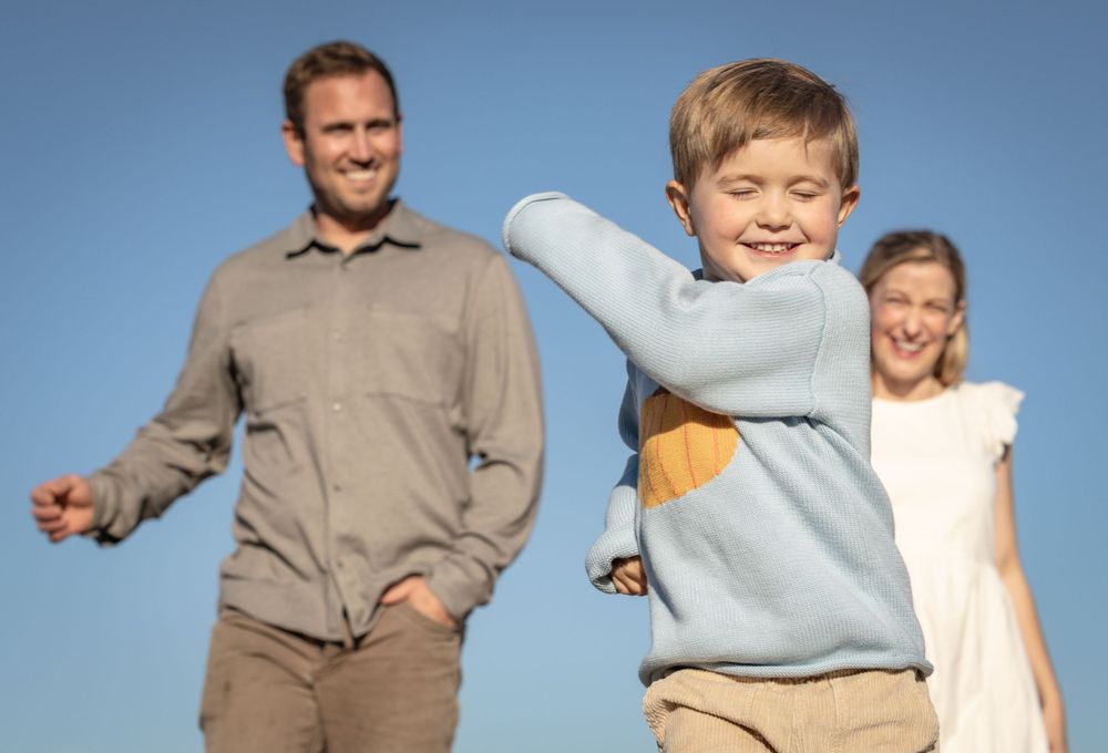 A family plays together outdoors against a bright blue sky background on a sunny day.
