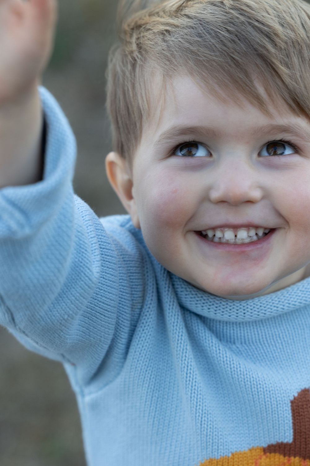 A child wearing a light blue sweater smiles brightly with an upward glance in a candid portrait.