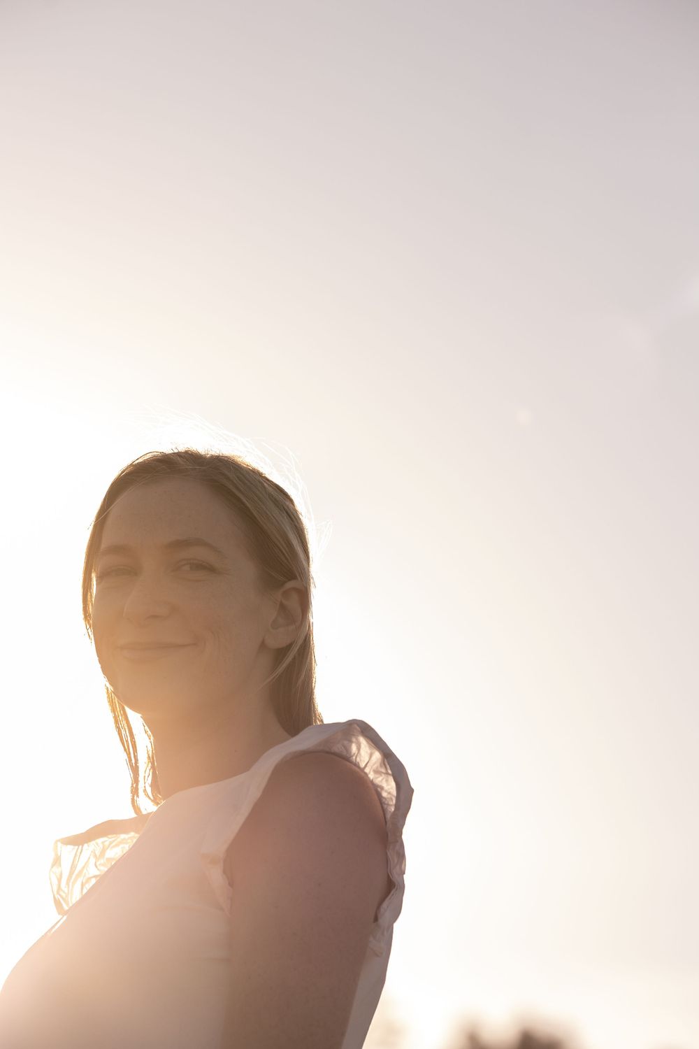 A silhouetted figure smiling against bright sunlight in a peaceful backlit portrait during golden hour.