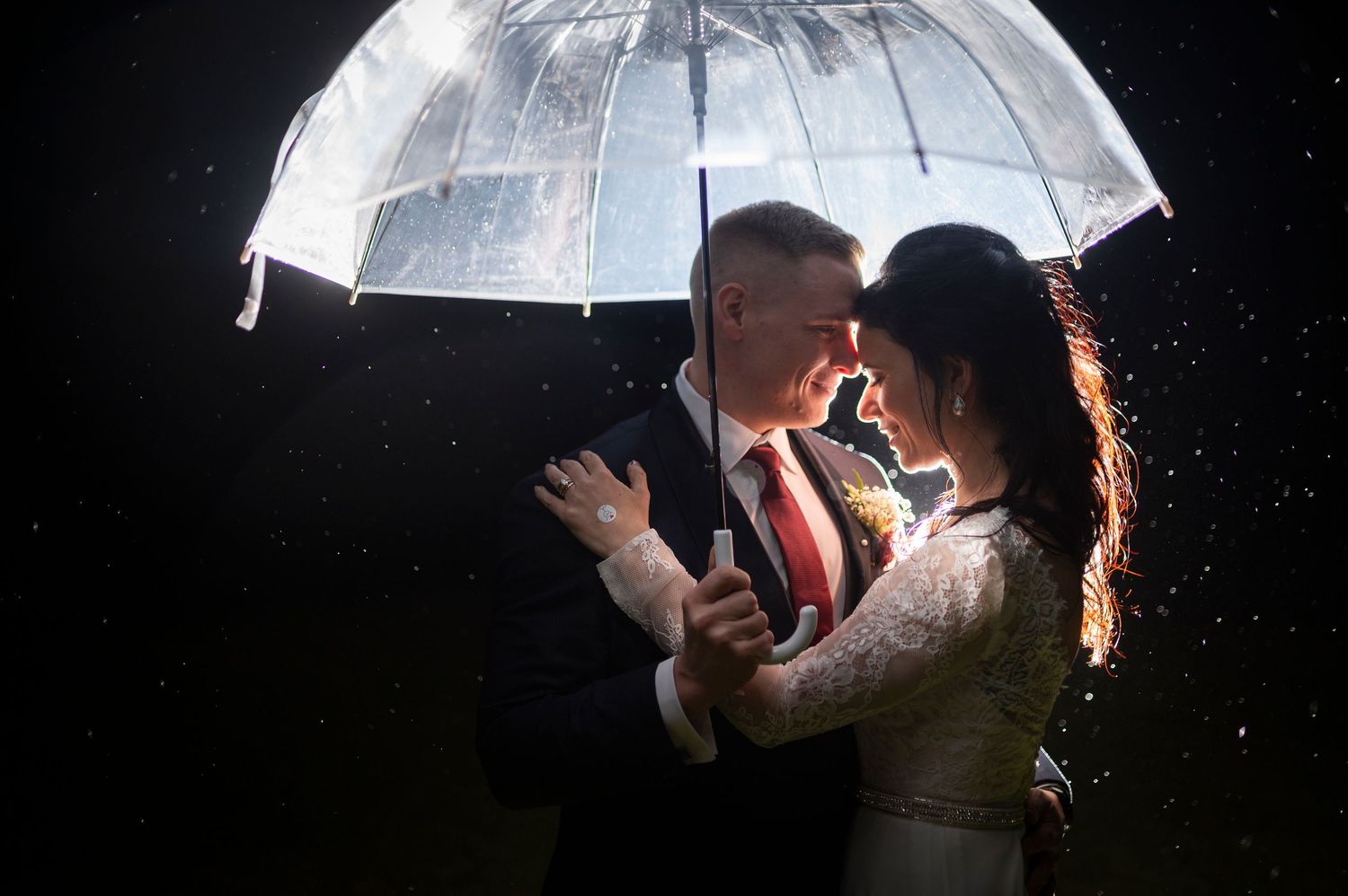 A couple shares an intimate embrace under a glowing umbrella in the rain at night.